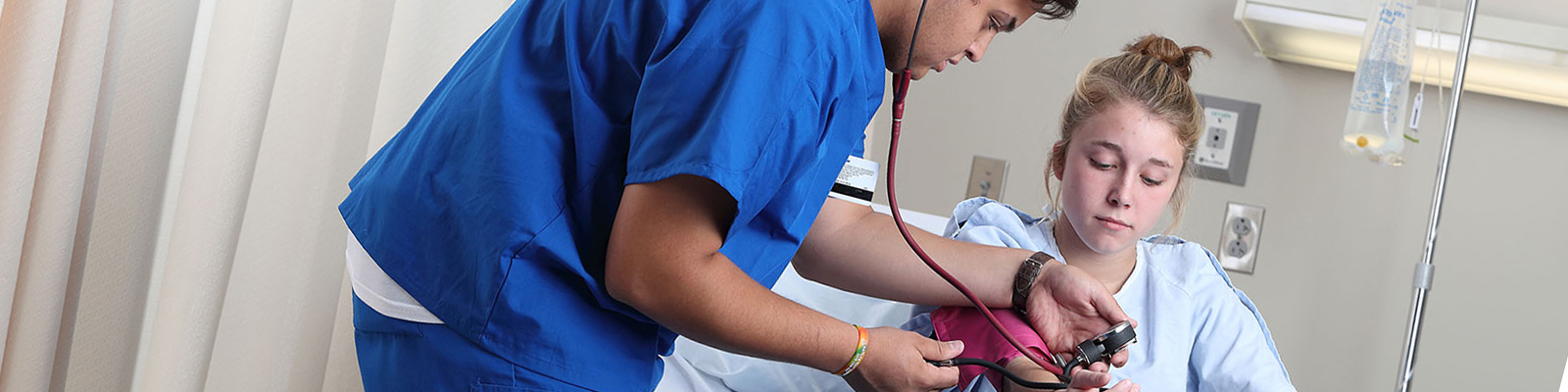 Male student in hospital room checking blood pressure on young female