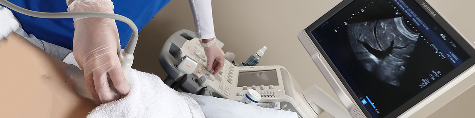 Student performing abdominal exam on patient with sonography machine, looking at screen