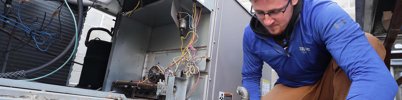 Student kneeling with wrench beside open AC unit