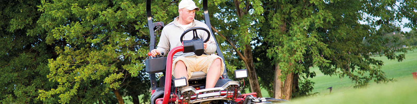 Man on large riding lawnmower, trimming grass on a golf course