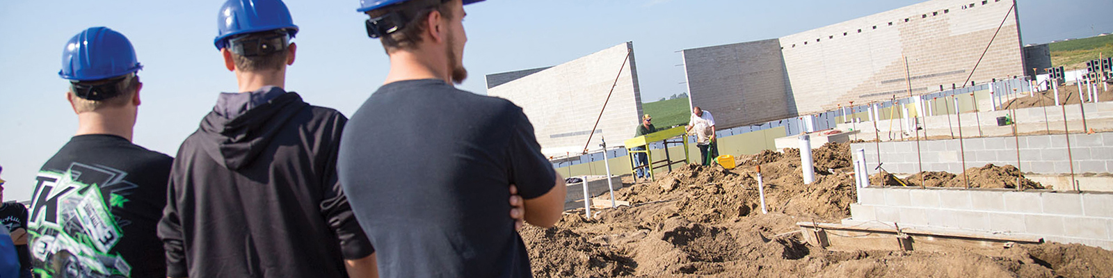 Students in blue hard hats facing away, looking at building site