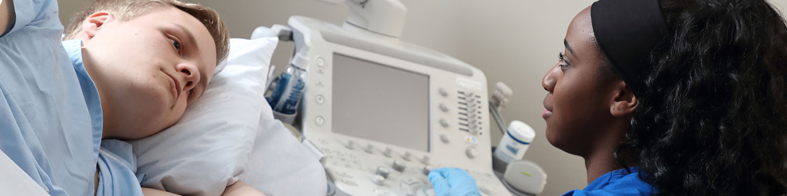 Student in scrubs using sonography machine on student patient