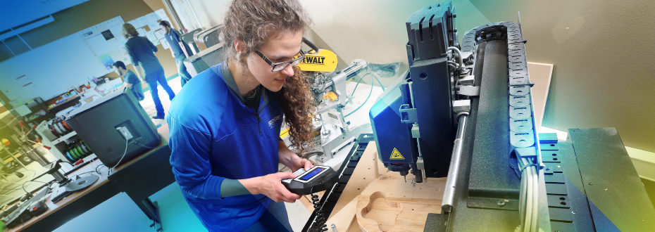 Male student in front of 3D printer, making adjustments in room full of 3D printers